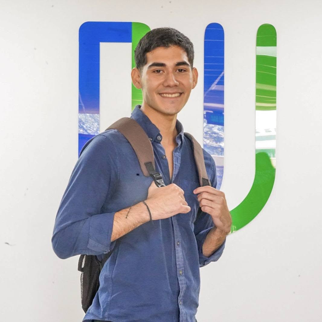 Estudiante con mochila sonriendo frente al logo de la UPES