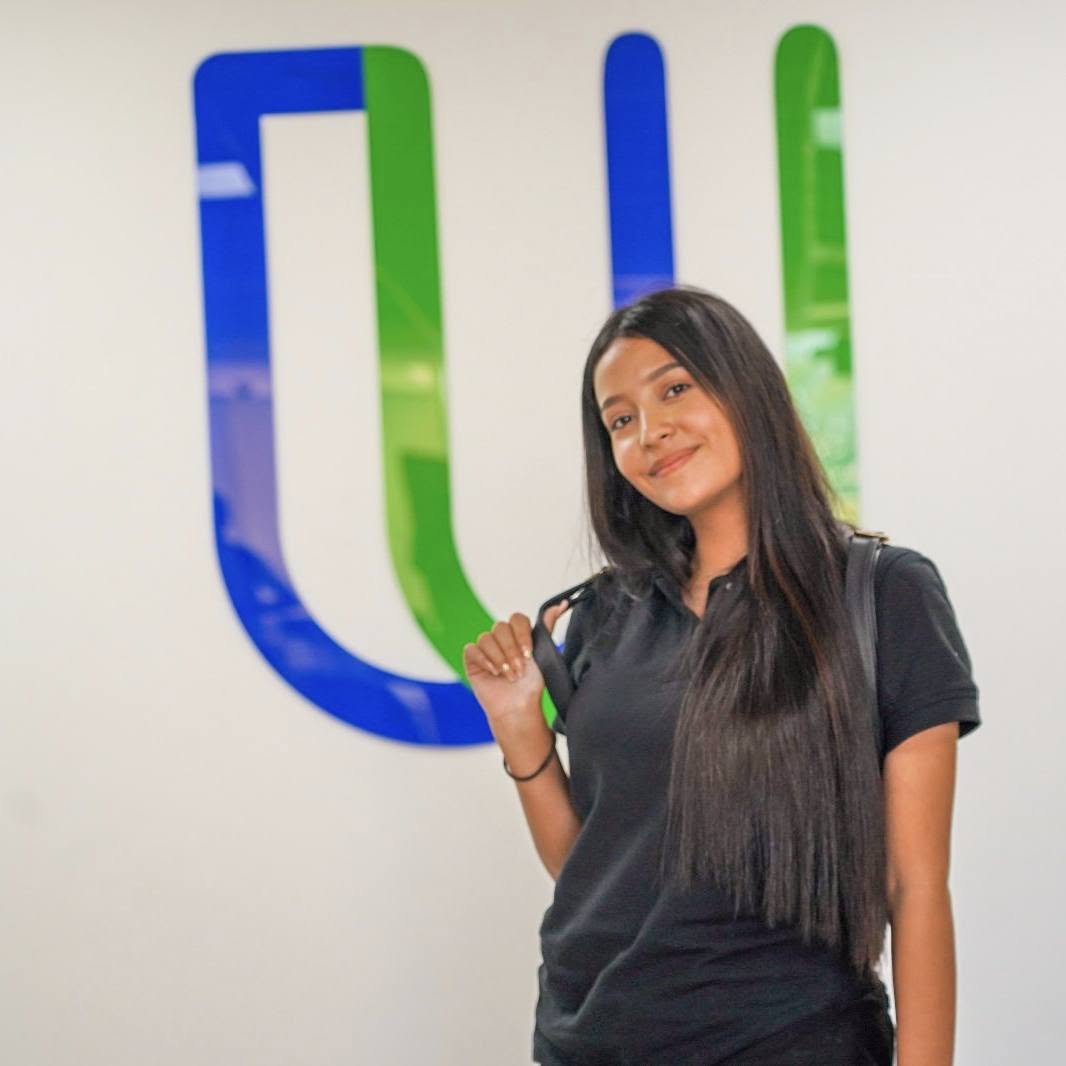 Estudiante sonriendo frente al logo de la UPES