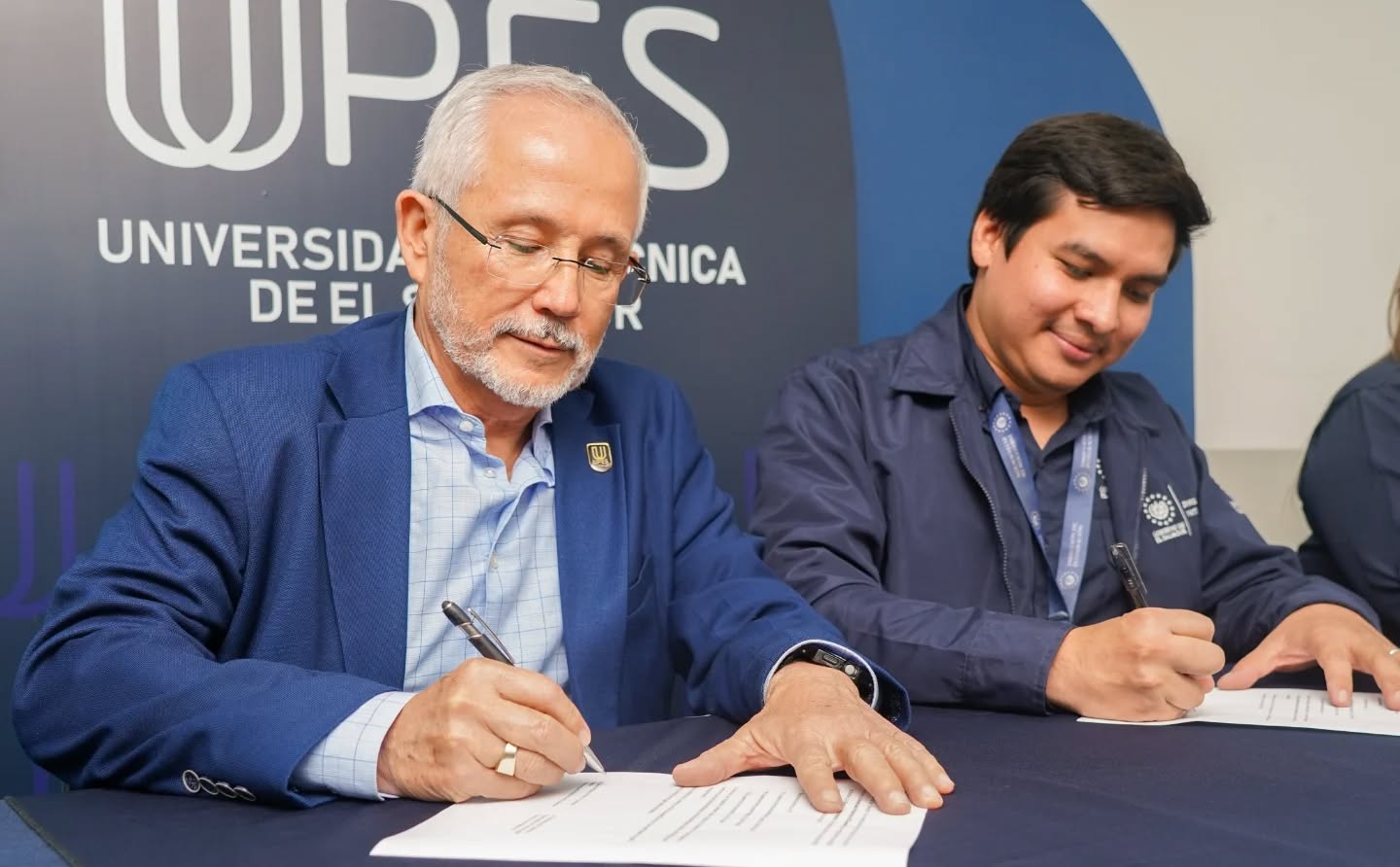 Firma de un convenio de cooperación frente al logo de la UPES